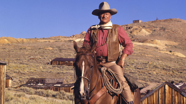John Wayne on horseback with a cowboy outfit on.