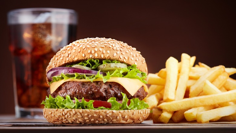 Cheeseburger with glass of cola and pile of french fries on wooden table