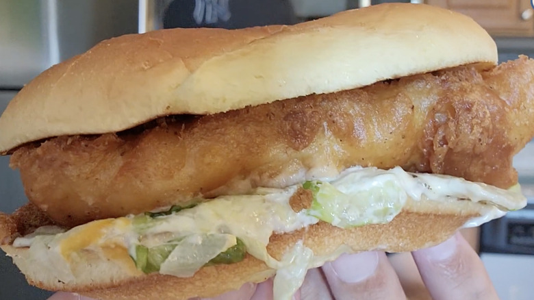 Hand holding up large fish sandwich to camera.