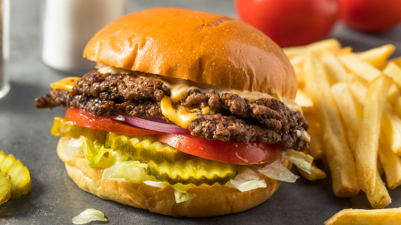 Fully loaded double smashburger with cheese next to fries on a countertop.