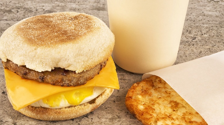 A fast food breakfast meal with coffee, hashbrowns, and sausage and egg muffin.