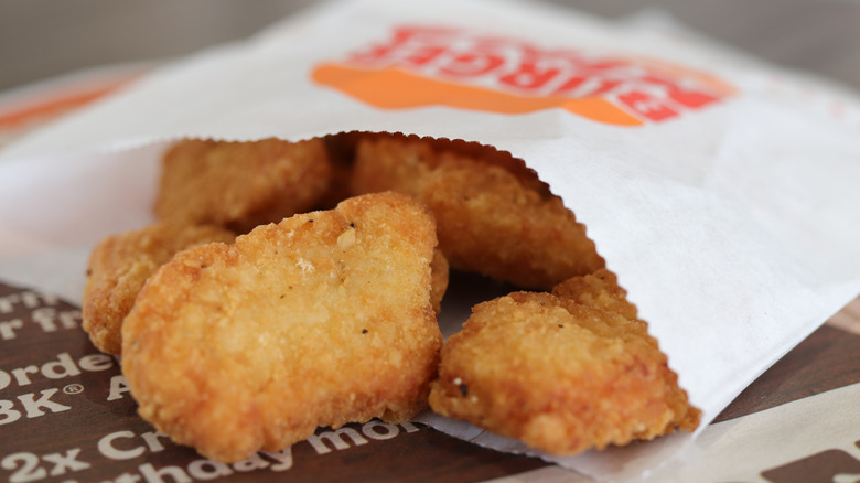 Chicken nuggets spilling out of a white paper sleeve with the Burger King logo