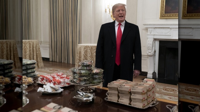 President Donald Trump standing behind a table covered with fast food items inside the White House in 2019