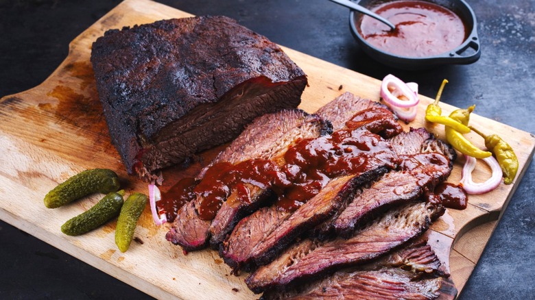 Smoked brisket on a cutting board with pickles and barbecue sauce