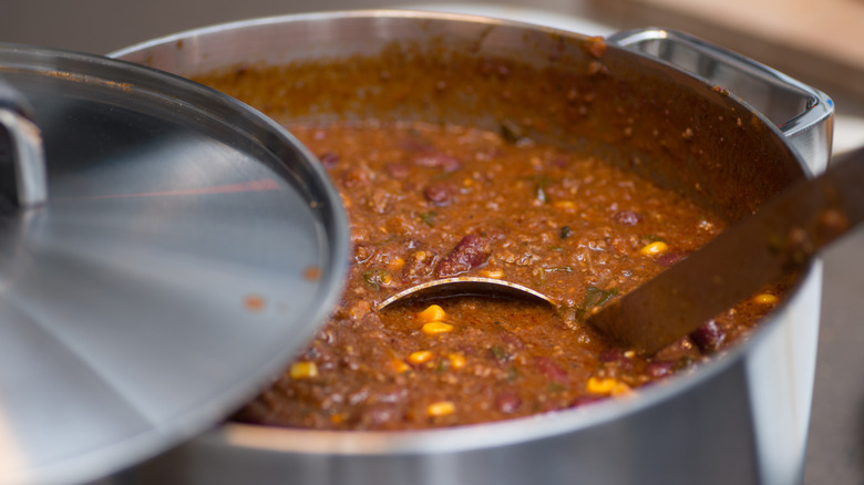 Chili in a large steel pot with a ladle inside of it