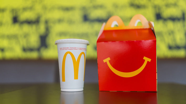 Mcdonald Happy meal with smile on box and beverage. McDonalds kids happy meal box set packaging, yellow background on black table with drink.