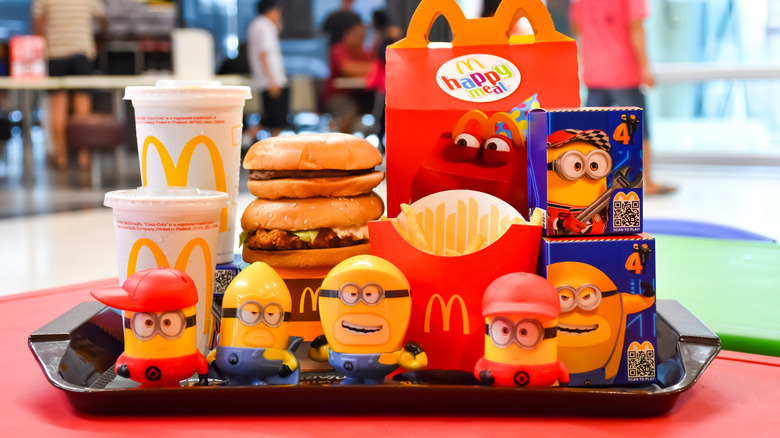 An array of McDonald's products, including a Happy Meal and Minions-related toys, on a tray in a McDonald's location