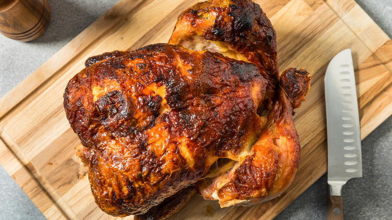 Rotisserie chicken on wooden cutting board next to knife
