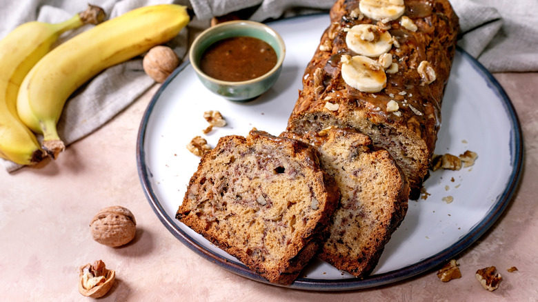 Sliced banana bread on a plate with caramel sauce and fresh bananas