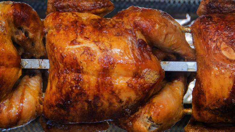 Rotisserie chicken on spit inside oven.