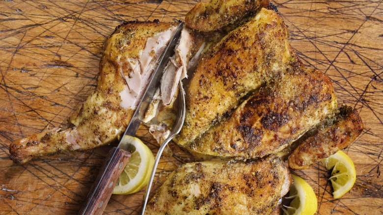 Roasted lemon pepper chicken on well-used cutting board with fork and knife.