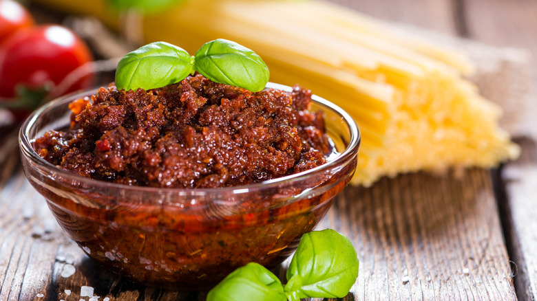 Sun-dried tomato pesto in glass bowl with baby basil on top.