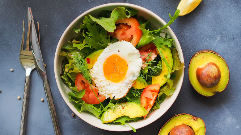 Top view of green salad with tomatoes, avocado, and fried egg