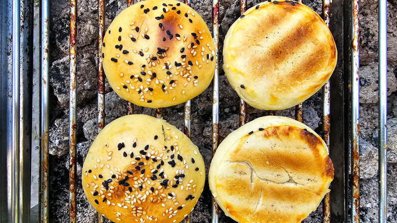 Two sesame seed bun halves on a grill
