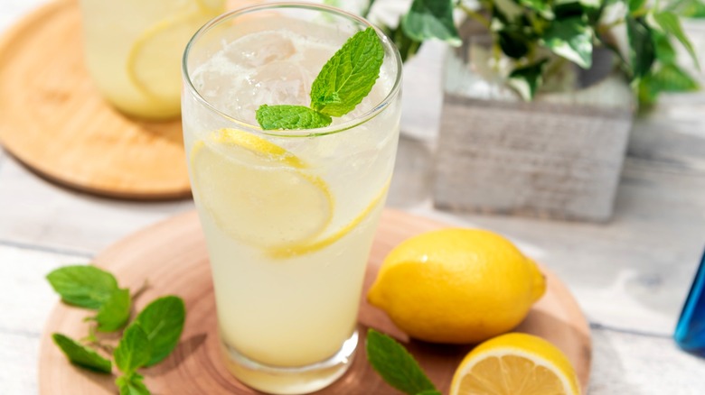 A glass of lemonade with ice, fresh mint, and lemons