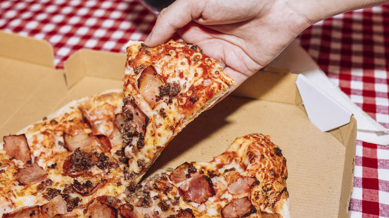 A person pulling a slice of pizza from a pie