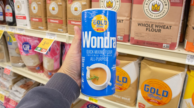 A hand holding a blue container of Wondra Quick-Mixing Flour in a grocery store