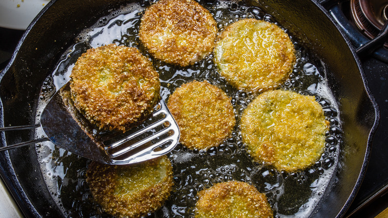 Fried green tomatoes frying in oil in a black skillet