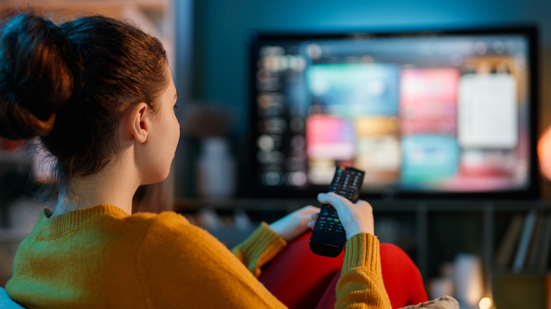 A young woman sits on a couch watching television.