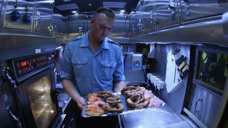 A submarine crew member holding a tray of food in the galley