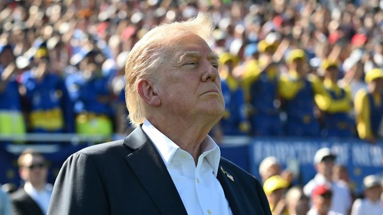 Donald Trump at a daytime sporting event with spectators behind him.