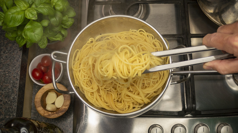 Spaghetti noodles being removed from a pot, surrounded by tomatoes, basil, and garlic