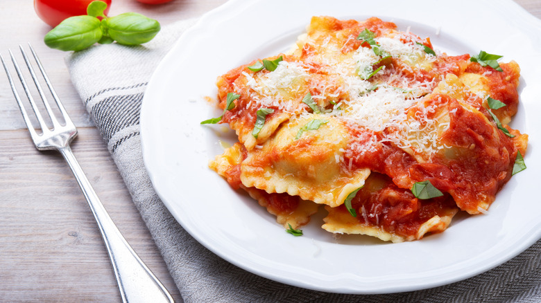 Ravioli with tomato sauce, grated cheese, fresh basil, and a fork