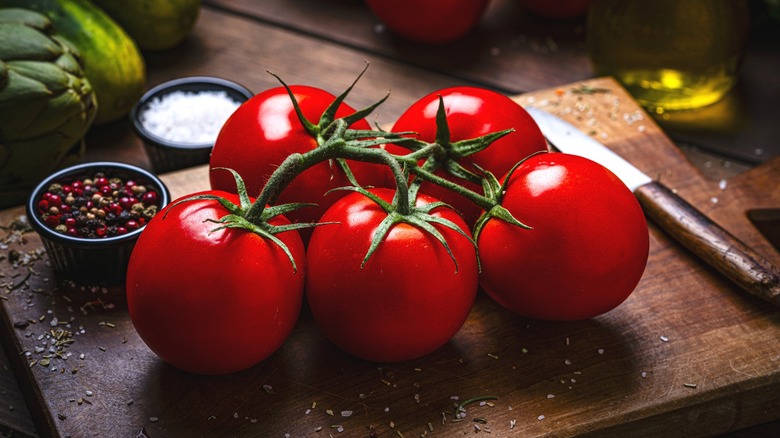 On-the-vine tomatoes on wood cutting board with knife