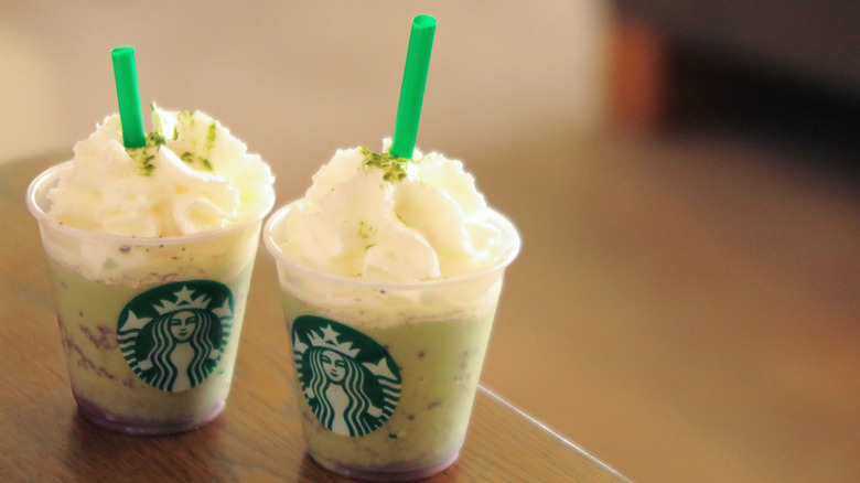 Two small cups of starbucks cold drinks with whipped cream and straws