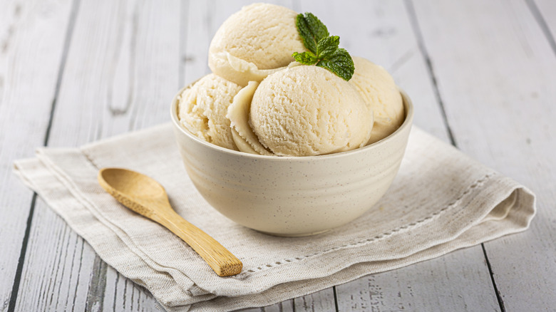 bowl of French vanilla ice cream garnished with mint leaves sitting on a beige cloth napkin next to a wooden spoon