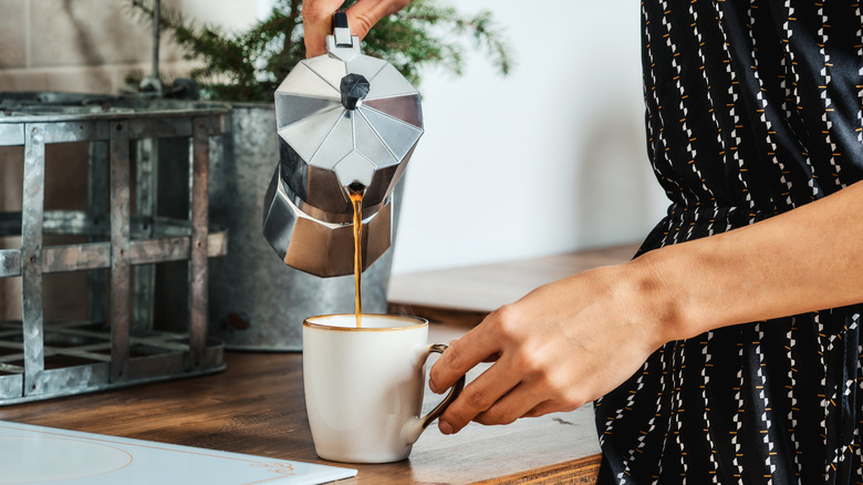 Person pouring coffee into a mug at home.