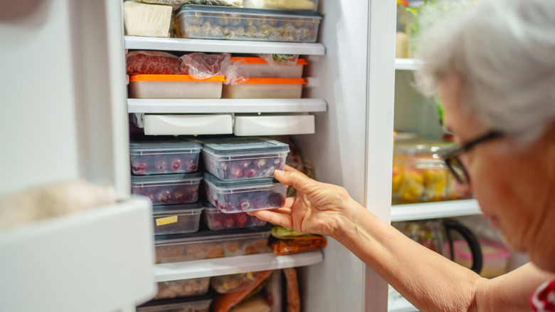 A woman reaches into an organized freezer, with neatly stacked containers