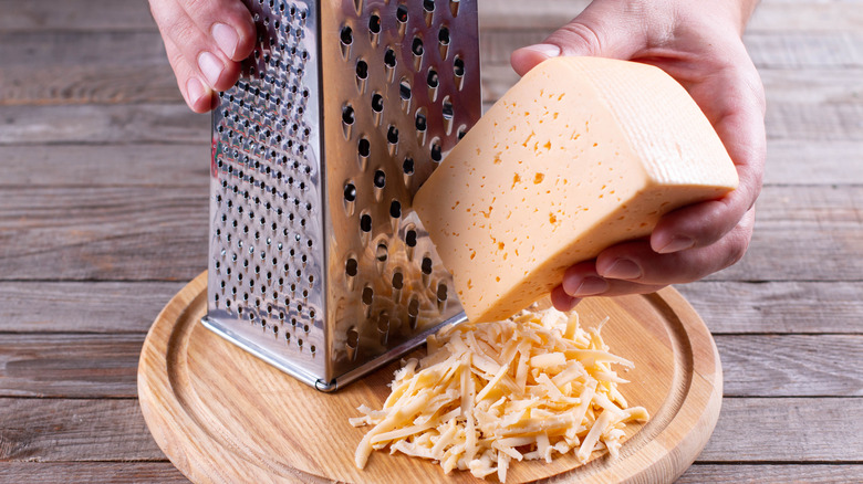 Hands grating a block of cheese on a box grater