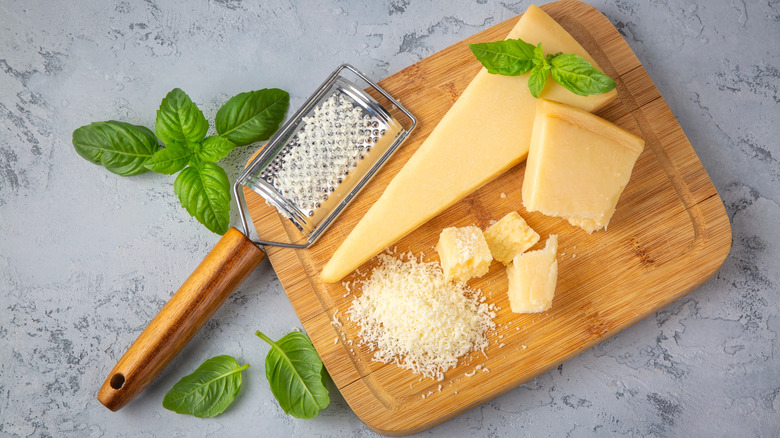 Wooden cutting board with wedge of parmesan cheese, grater, and grated parmesan cheese