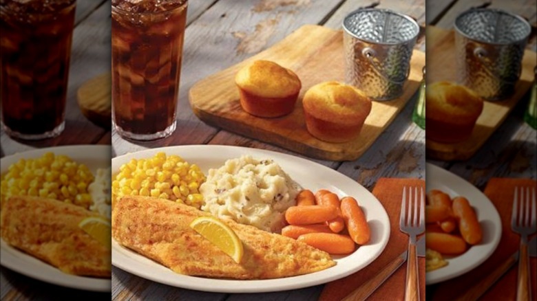 A plate of Cracker Barrel's haddock dinner with all the sides on a farmhouse table near a soda and utensils