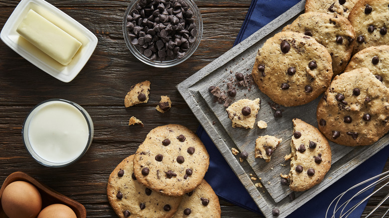 Chocolate chip cookies on a wooden platter with eggs, butter, milk, and chocolate chips