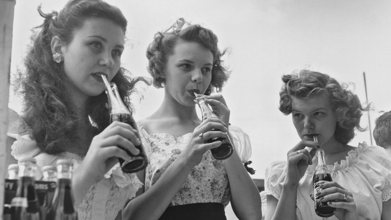 Three young women drinking soda from a straw in black and white