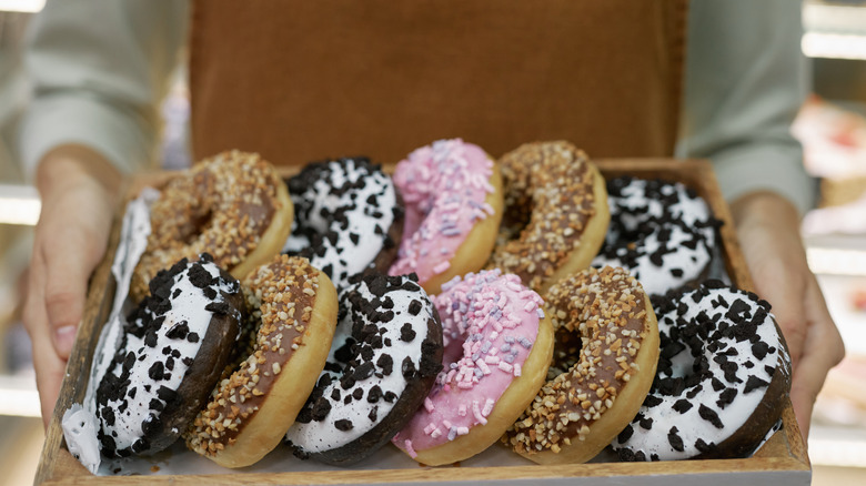 worker holds tray of iced donuts with toppings