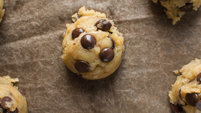 A ball of chocolate chip cookie dough on parchment paper