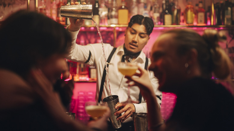 A bartender makes a drink as two patrons talk to each other