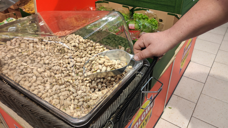 Person scooping out pistachios from the bulk bin at a grocery store