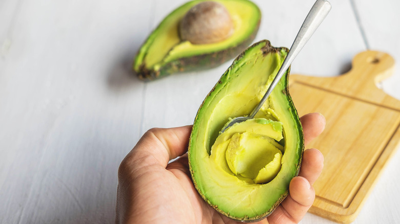 Person holding half an avocado as the flesh is scooped out
