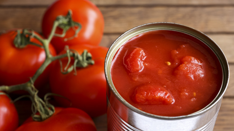 Open tin of chopped tomatoes with whole fresh unfocused tomatoes beside it.
