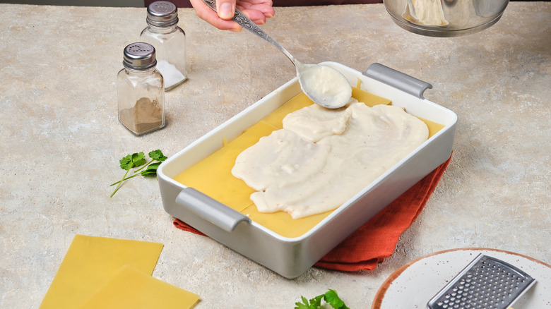 Spoon spreading béchamel sauce in lasagna