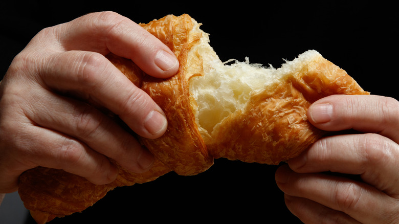 Person's hands tearing into a croissant