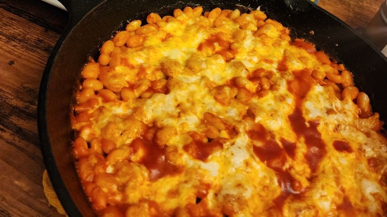 Cheesy baked beans sitting on a black plate.