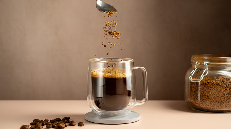 spoon pouring instant coffee granules into cup of coffee