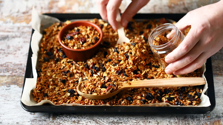 Hands scooping granola from sheet pan into jar
