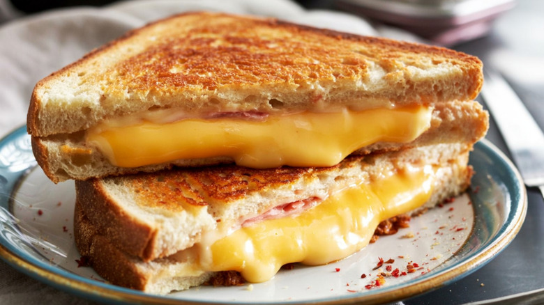 A grilled cheese sandwich with ham inside sitting on a plate with melty cheese pouring out
