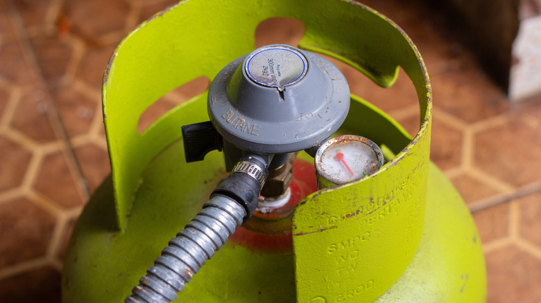 Close-up of a green LPG gas cylinder with pressure regulator and hose on tiled floor.